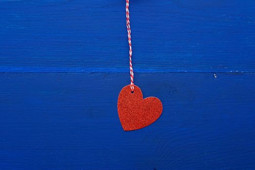 paper red shiny decorative hearts hanging on a rope on a dark blue wooden background, abstract holiday backdrop for valentines day on february 14. Decoration element