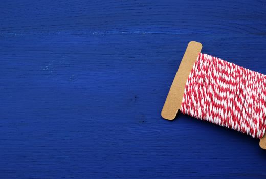 skein of craft red-white thread on a blue wooden background, backdrop or banner for needlework, copy space