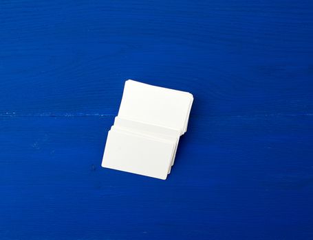 stack of white blank paper rectangular business cards on blue wooden background, template for designer
