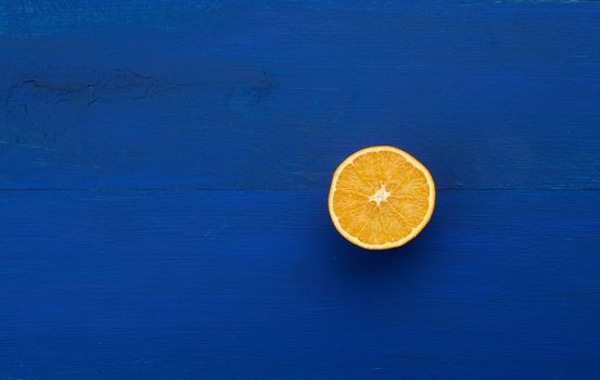 half ripe juicy orange on a dark blue wooden background, abstract trendy backdrop with fruit in a minimalist style
