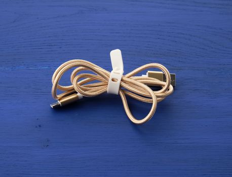 twisted golden cable for charging with electricity equipment in textile winding on a blue wooden background, close up