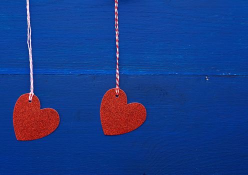paper red shiny decorative hearts hanging on a rope on a dark blue wooden background, abstract holiday backdrop for valentines day on february 14