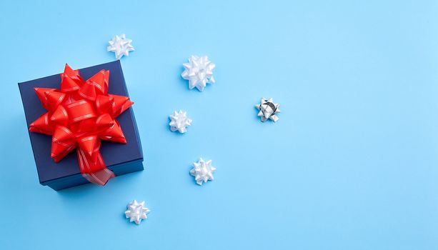 dark blue cardboard gift square box, red bow, ribbons on a blue background, top view. Festive concept