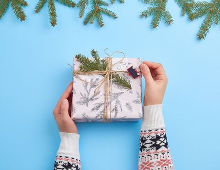two female hands holding a gift wrapped in festive wrapping paper on a blue background, top view