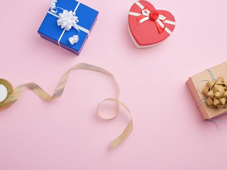 square gift boxes decorated with ribbons and bows on a pink background, top view, place for text