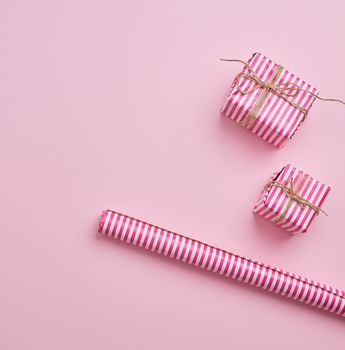 two gifts wrapped in pink striped paper and paper roll on a pink background, top view, copy space