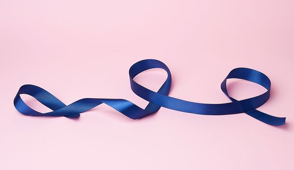 dark blue silk ribbon twisted into loops on a pink background, abstract background for the designer