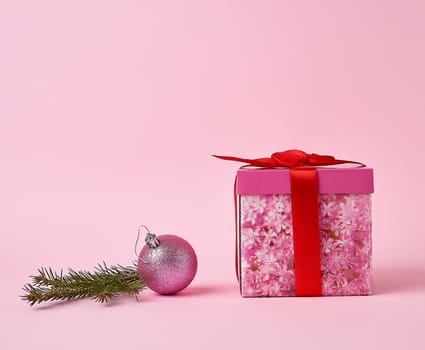 pink gift box with bow, green spruce branch and decorative pink ball on a pink background