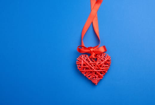 red wicker decorative heart hanging on silk ribbon, blue festive background for Valentine's day, copy space