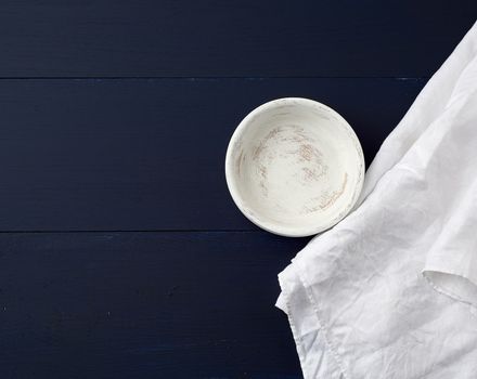 round wooden plate and white linen towel on blue wooden background, top view, copy space