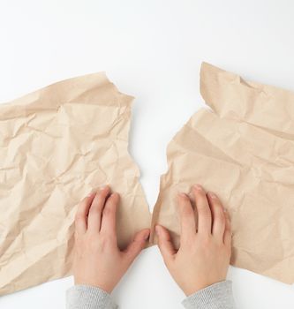 two hands tearing a sheet of brown craft paper, top view