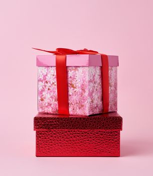 square cardboard pink box tied with a red bow on a pink background, holiday background 