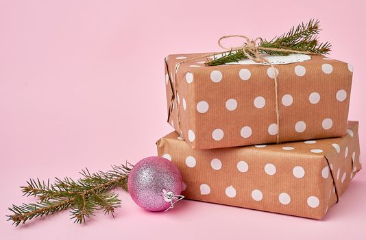 stack of kraft paper wrapped gifts, spruce branch on pink background. Christmas greeting concept