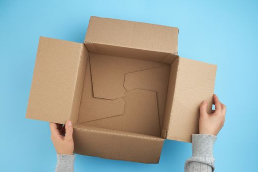two female hands holding an empty open box of brown cardboard, at the bottom there is a white foam for packaging, top view, concept of packing things