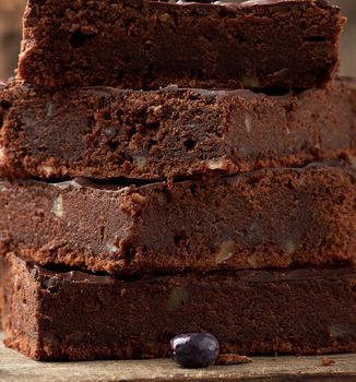 stack of square baked slices of brownie chocolate cake with walnuts on a wooden surface. Cooked homemade food. Chocolate pastry. Sweet meal, homemade dessert. Wooden table.