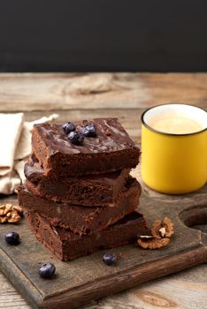 stack of square baked slices of brownie chocolate cake with walnuts on a wooden surface. Cooked homemade food. Chocolate pastry. Sweet meal, homemade dessert. Wooden table.