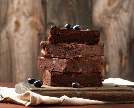 stack of square baked slices of brownie chocolate cake with walnuts on a wooden surface. Cooked homemade food. Chocolate pastry. Sweet meal, homemade dessert. Wooden table.