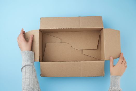 female hands are holding an empty open box of brown cardboard, top view, concept of packing things