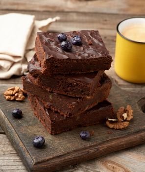 stack of square baked slices of brownie chocolate cake with walnuts on a wooden surface. Cooked homemade food. Chocolate pastry. Sweet meal, homemade dessert. Wooden table.