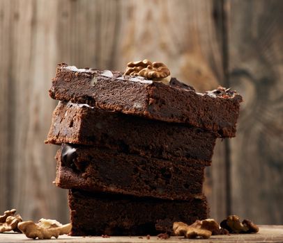 stack of square baked slices of brownie chocolate cake with walnuts on a wooden surface. Cooked homemade food. Chocolate pastry. Sweet meal, homemade dessert. Wooden table.