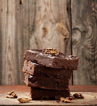 stack of square baked slices of brownie chocolate cake with walnuts on a wooden surface. Cooked homemade food. Chocolate pastry. Sweet meal, homemade dessert. Wooden table.