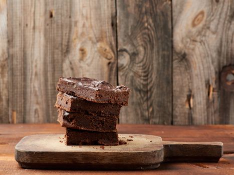 stack of square baked slices of brownie chocolate cake with walnuts on a wooden surface. Cooked homemade food. Chocolate pastry. Sweet meal, homemade dessert. Wooden table