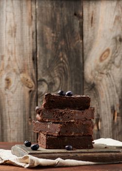 stack of square baked slices of brownie chocolate cake with walnuts on a wooden surface. Cooked homemade food. Chocolate pastry. Sweet meal, homemade dessert. Wooden table.
