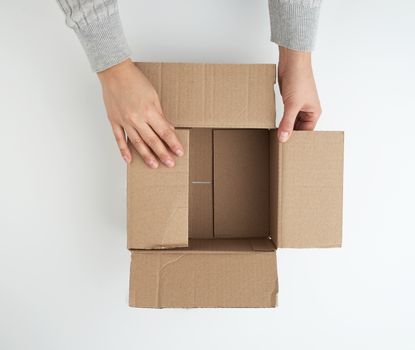 open empty square brown cardboard box for transportation and packaging of goods and two hands, view from the top