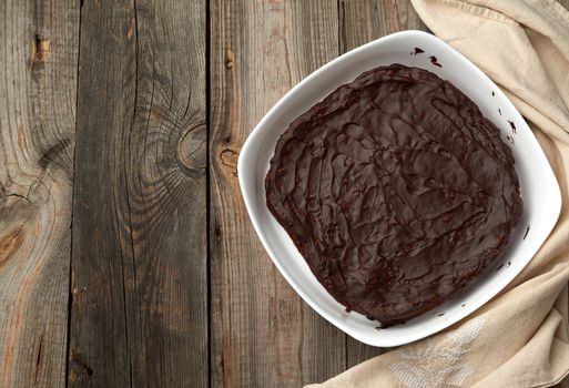 baked brownie chocolate cake in a white ceramic plate on a gray wooden background, top view, place for text.  Cooked homemade food. Chocolate pastry. Sweet meal, homemade dessert. Wooden table.