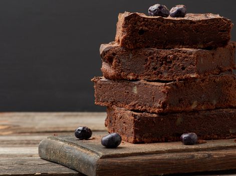stack of square baked slices of brownie chocolate cake with walnuts on a wooden surface. Cooked homemade food. Chocolate pastry. Sweet meal, homemade dessert. Wooden table.