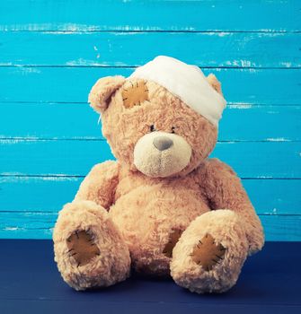 sad brown bear sits with bandaged white medical bandage head, injury and headache concept