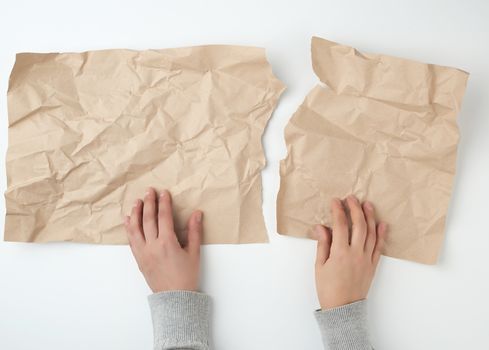 two hands tearing a sheet of brown craft paper, top view