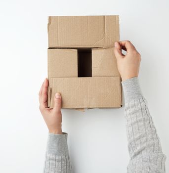 two female hands close a square brown cardboard box on a white background, concept of moving and delivery of goods