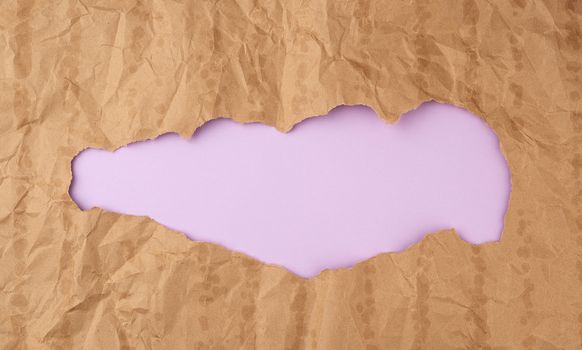 crumpled paper texture from a brown sheet of paper with greasy spots and a large hole. abstract banner for the designer, purple backdrop. 