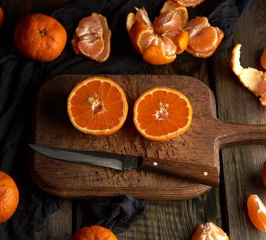 ripe round tangerines and cut in half on an old vintage cutting board. Healthy vegetarian food. Citrus fruit.