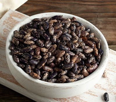 raw oval red marble beans in a plate on a wooden table. Agriculture harvest. Vegetarian healthy natural food.