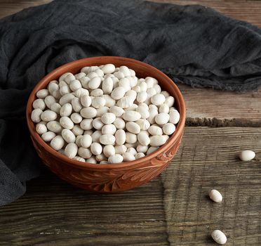 raw round white beans in a plate on a wooden table. Organic meal. Vegetarian healthy natural food.
