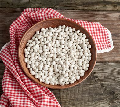 raw round white beans in a plate on a wooden table. Organic meal. Vegetarian healthy natural food.
