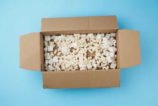 open rectangular brown cardboard box with white foam filling for transporting goods on a blue background, top view