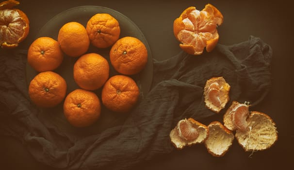 round ripe tangerines in a plate on a black textile napkin, top view, low key