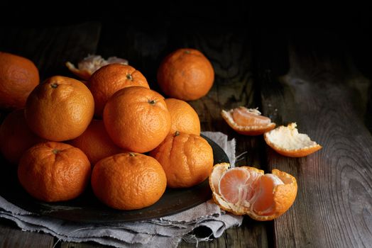 heap of unpeeled round ripe orange mandarin on a gray linen napkin, wooden table, low key
