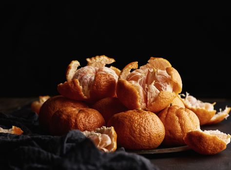 heap of round ripe tangerines in a plate on a black textile napkin, low key