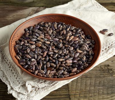 raw oval red marble beans in a plate on a wooden table. Agriculture harvest. Vegetarian healthy natural food.