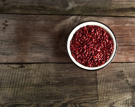 raw oval red beans in a plate on a wooden table. Organic meal. Vegetarian healthy natural food.