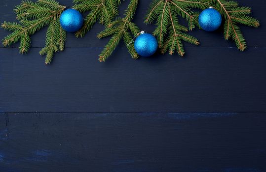 green spruce branches and dark blue shiny Christmas balls on a blue wooden background from boards, festive backdrop for Christmas and New Year, place for an inscription