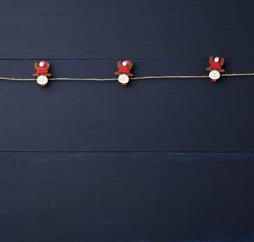 decorative holiday clothespins with a figure of a deer hang on a brown rope, blue wooden background