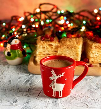 red ceramic cup with black coffee. near green branches of spruce and christmas toys. Christmas season beverage.