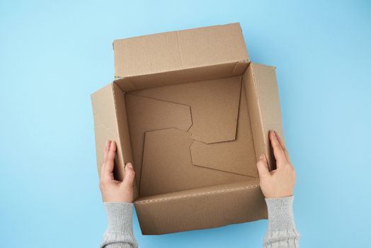 two female hands are holding an empty open box of brown cardboard, top view, the concept of packing things