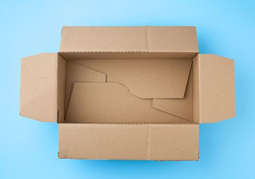 open empty square brown cardboard box for transportation and packaging of goods on blue background, top view.