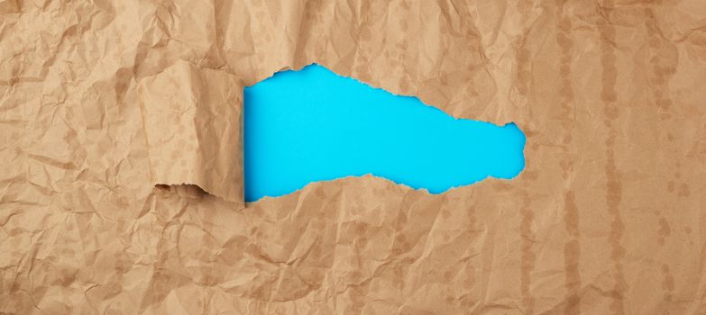 crumpled paper texture from a brown sheet of paper with greasy spots and a large hole with a twisted corner, abstract banner for the designer, blue backdrop. Vintage template with brown paper hole curling  